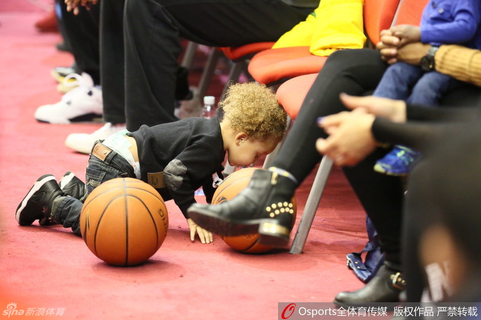 小儿子张开双臂与哥哥争宠，踮起脚尖想要亲吻哥哥手中的篮球，兄弟俩的可爱互动让身后的妈妈也忍俊不禁