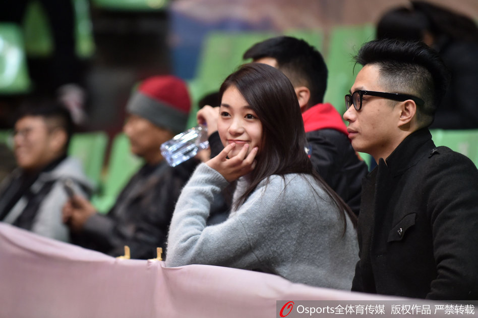 赛场灯光下，一位戴着精致发卡的女孩双手轻托脸颊，目光专注地望向场内，嘴角带着一丝期待的微笑，安静地等待着比赛的精彩时刻。