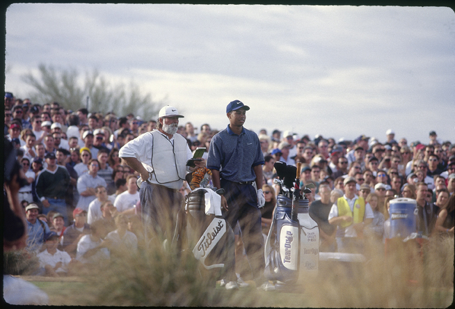 球手与球童并肩而立，低头专注地研判球道攻略，每一次成功的背后都是团队的智慧。