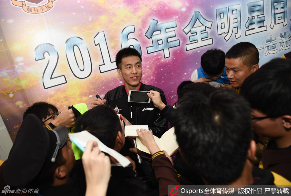 辽宁球星郭艾伦身穿北区蓝色球衣，被一群热情的球迷团团围住，他脸上笑开了花，眼睛眯成一条缝，正低头为一位球迷手中的纪念品签名。