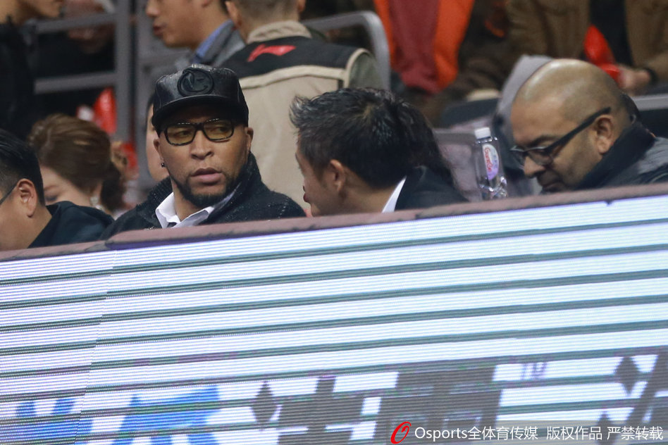 比赛暂停期间，马里昂侧身与身旁的一位工作人员交谈，他眉头微蹙，似乎正在交流着对场上球员表现的看法，背景是喧嚣的球场。