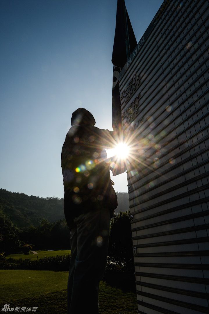 广州南沙高尔夫球会绿意盎然的球场全景，球道与湖泊交错，远处山峦起伏，构成一幅静谧而富有挑战性的竞技画卷。