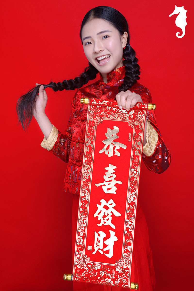 身穿精致刺绣唐装的宝贝眼神俏皮地斜瞥一侧，嘴角微翘，一副精灵古怪的机灵样，仿佛在琢磨着新年捣蛋的小计划