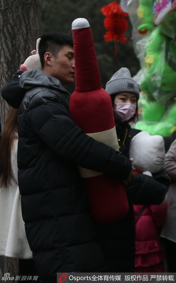 常林与女伴在一个售卖传统工艺品的地坛庙会摊位前选购，他微微低头倾听女伴的话语，205厘米的身高在人群的映衬下宛如巨人，画面充满了温馨的日常气息。