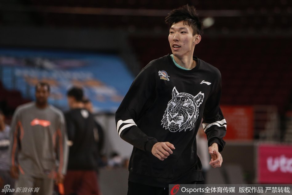 主教练李秋平双手叉腰站在场边，神情严肃地注视着球员们的训练，嘴里不时喊着战术指令