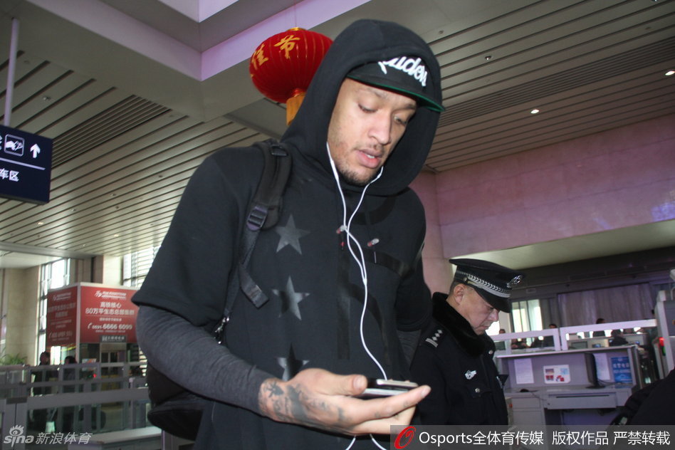 身穿红色外套的比斯利在高铁站入口处被热情球迷团团围住，他面带微笑耐心地俯身为身前的小球迷在篮球上签名，场面温馨动人。