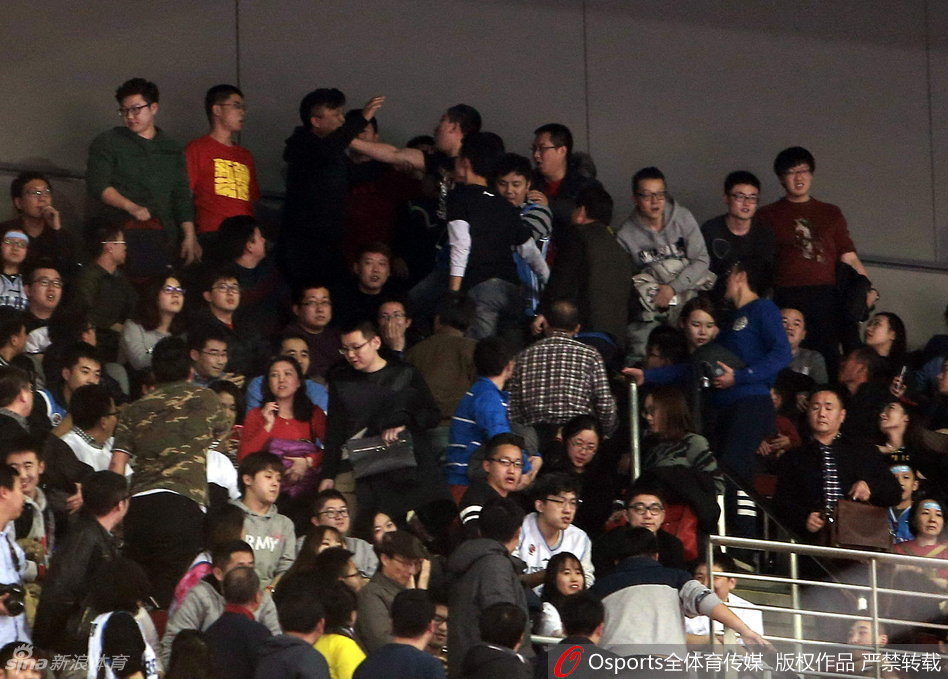 身穿白色背心的北京球迷情绪失控，探出半个身子越过看台围栏，手臂直指向场地中央，脸上写满了不甘与愤怒，似乎在向场内的工作人员咆哮申诉。