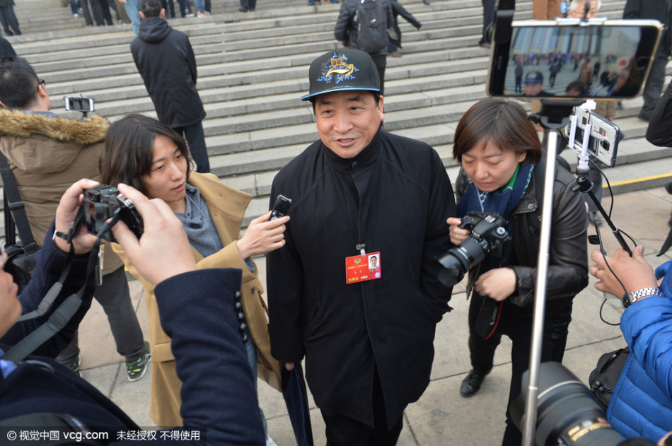 春日的阳光洒在人民大会堂台阶上，姜昆面带标志性的微笑，头顶蓝色北京冠军帽信步走来，眼神中透出履职的从容与自信。