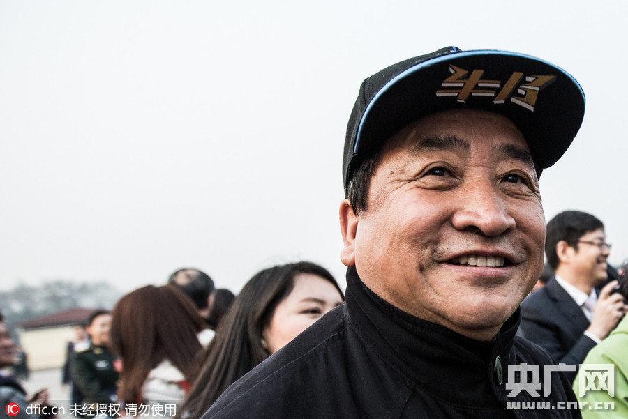 面对簇拥的话筒与录音笔，姜昆身体微微前倾专注倾听记者提问，神情平和亲切，那顶醒目的北京冠军帽在镜头中成为最独特的背景。