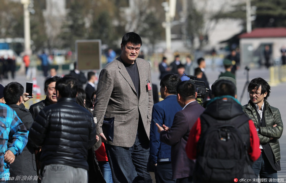 在人群的簇拥下，巨人姚明微微低头，仿佛一座移动的铁塔，从层层包围的记者缝隙中艰难地向大会堂入口移动。