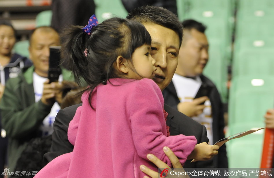 女儿伸出小手似乎想触摸什么，郭士强则稳稳地托着她，父女俩在赛场边的互动充满了童趣与温情。