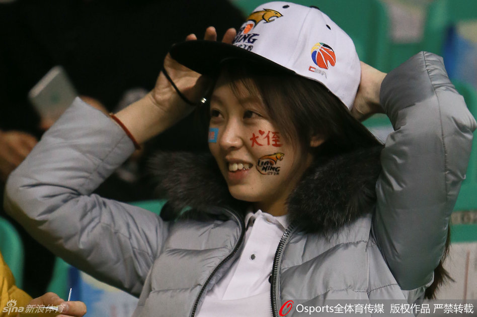 看台上一位气质出众的女球迷，眉眼间流露出对赛场局势的关切，她嘴角不经意间流露出的甜蜜微笑，仿佛一缕春风拂过紧张的赛场。