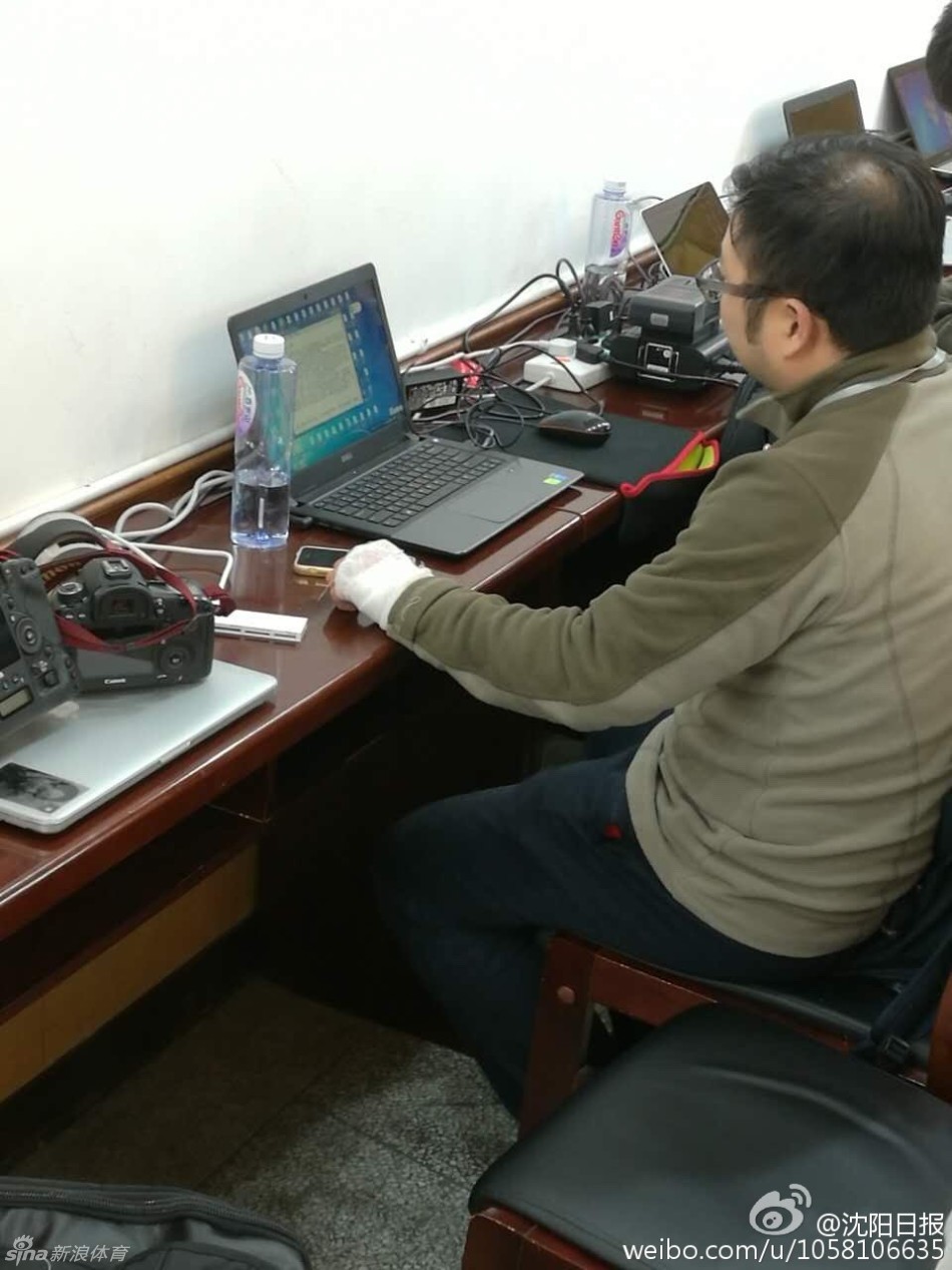 一位女记者正用缠着绷带的手指向电脑屏幕，似乎在与同事讨论稿件。白色的绷带与她专注工作的神情形成鲜明对比，仿佛在说：无论场外有多少纷扰，报道真相的手永远不会停歇。