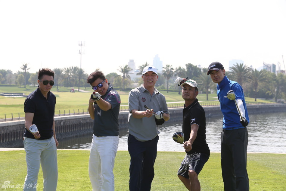 张连伟与友人或赛事官员在迪拜球场边微笑着交流，身旁停着高尔夫球车，氛围轻松融洽