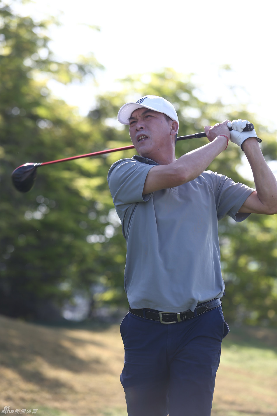 张连伟在球场上手持一支别致的烟斗，神情放松，尽显高尔夫运动的绅士风度与闲暇雅趣