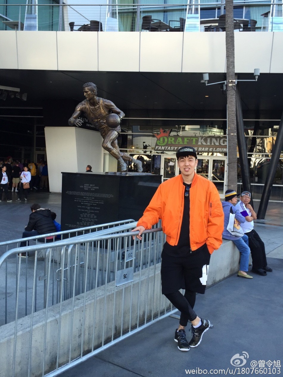 斯台普斯中心内场，曾令旭身穿醒目的科比24号球衣，举起手中的科比摇头娃娃，身后是即将见证历史的狂热球迷海洋