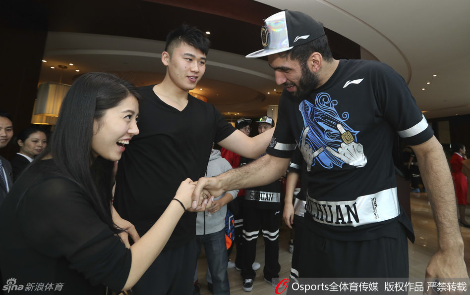 身穿制服的气质空姐化身小粉丝，在哈达迪身边仰头微笑，哈达迪则绅士地弯下腰，轻轻握住女球迷的手，画面温馨而有趣。