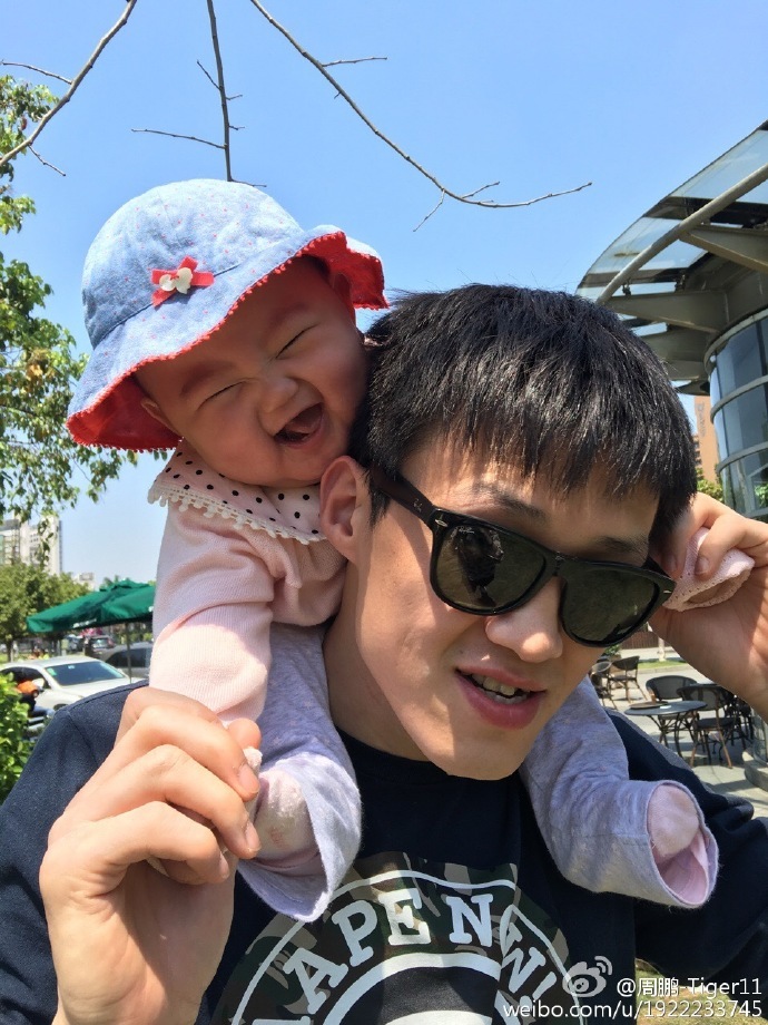 在温柔的阳光下，奶爸周鹏抱着他的小公主，两人脸贴着脸，爸爸眼中满是宠溺，小baby则笑得眼睛弯成月牙，画面温馨极了。