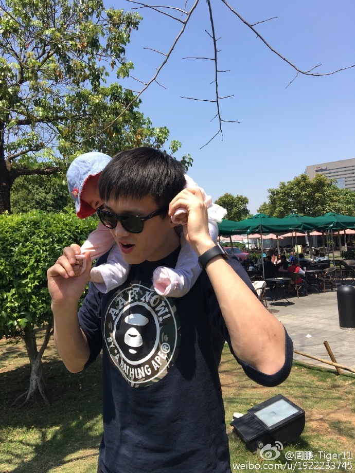 阳光透过树叶洒在父女俩身上，周鹏轻轻握着女儿的小手，小家伙则专注地低头研究着什么，画面静谧而美好，仿佛时间都为这份温柔停留。