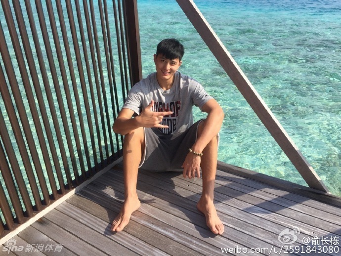 俞长栋穿着休闲夏装，在椰林树影下为妻子拍照，阳光透过树叶洒在他专注的脸上，这一刻他不是球星，只是一个记录妻子美丽的普通丈夫。