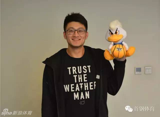 段江鹏加盟北京首钢后，面露羞涩而坚定的微笑，双手紧握象征京城荣耀的霹雳鸭吉祥物，仿佛握住了崭新的未来。