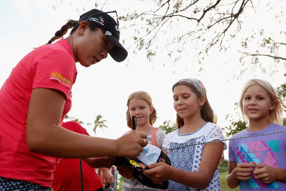 高宝璟弯下腰，微笑着为一位小粉丝在帽子上签名，画面充满暖意。