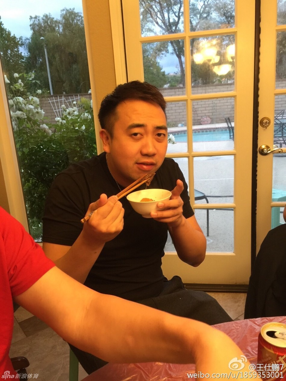 聚会尾声众人起身离席，易建联披着外套与王仕鹏勾肩搭背，刘宏疆在旁微笑，窗外夜色中洛杉矶灯火闪烁