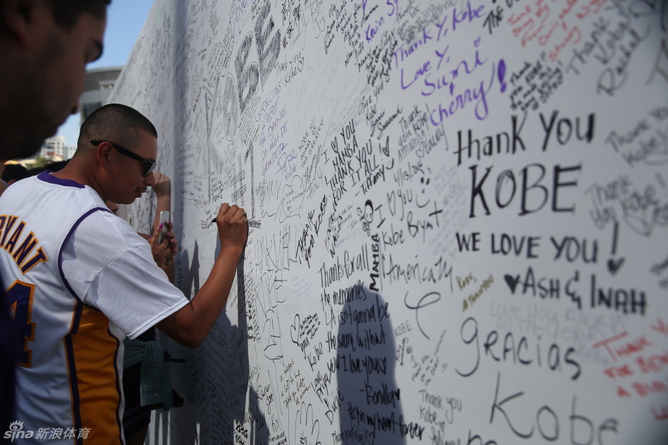 斯台普斯中心外，一位眼神清澈的小球迷穿着过大的科比球衣，手持加油标语，在父母的陪伴下静静等待偶像的最后一舞。