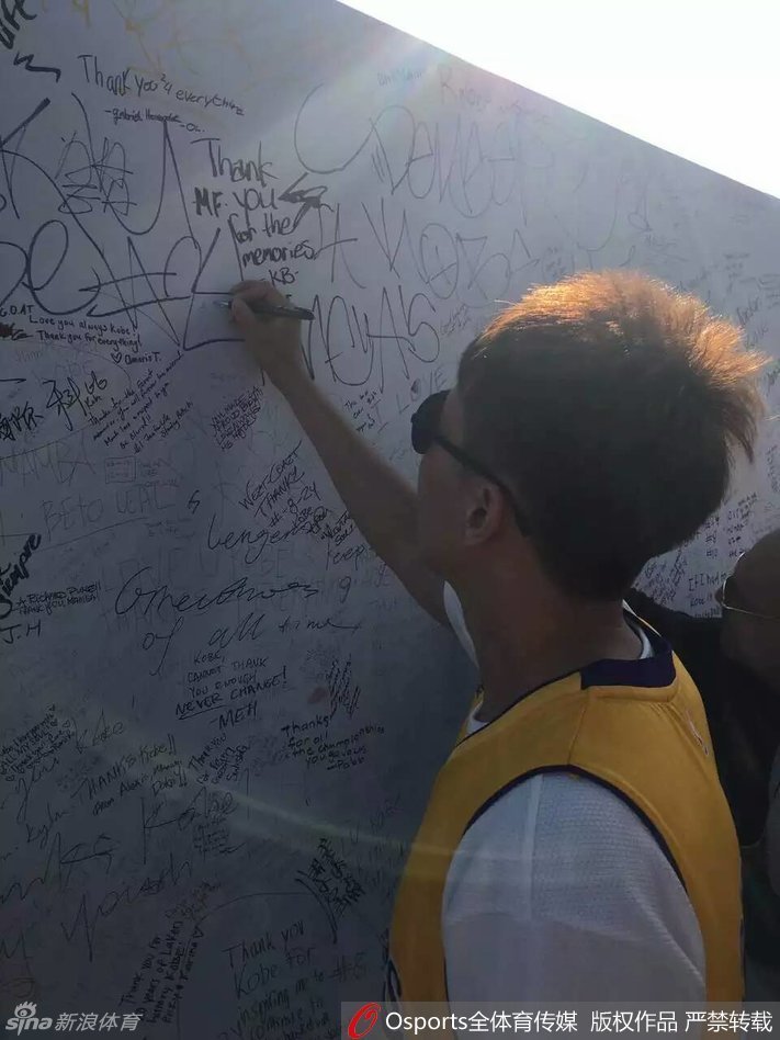 斯台普斯中心外，人潮涌动，曾令旭身穿醒目的紫金24号球衣，在科比的巨幅海报前停下脚步，眼神中满是期待与崇敬，用手机记录下这即将圆梦的一刻。