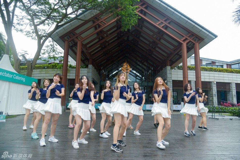 志愿者女孩们聚在休息区，对着镜头比出胜利手势，身后是繁忙而有序的赛事活动现场