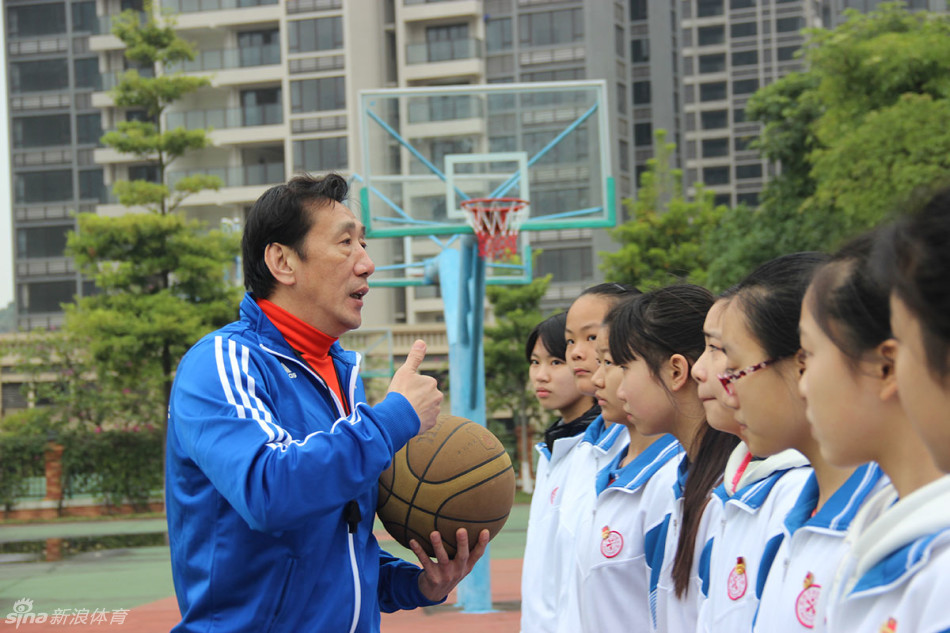 李群弯腰俯身纠正小队员的运球姿势，眼神专注，手把手教学