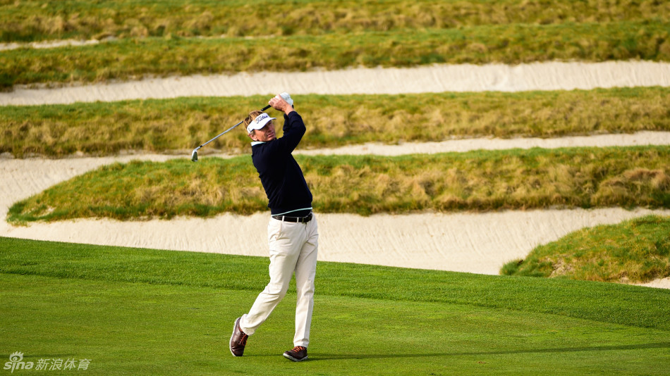 奥拉查宝与球童在球道中央认真讨论下一杆的策略，两人手指不同方向，背景是奥克蒙特蜿蜒的球道与远方林立的树木，展现团队作战的深思熟虑。