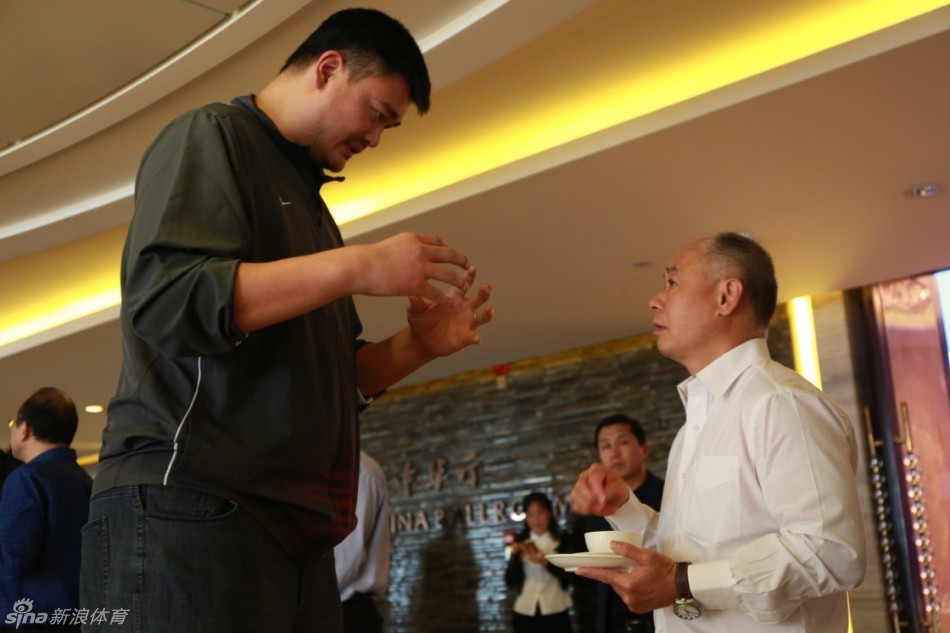 中国篮坛传奇巨星姚明与“体操王子”李宁在会场内握手交谈，两人巨大的身高差构成了一幅有趣的画面，李宁仰头望向姚明，相谈甚欢。