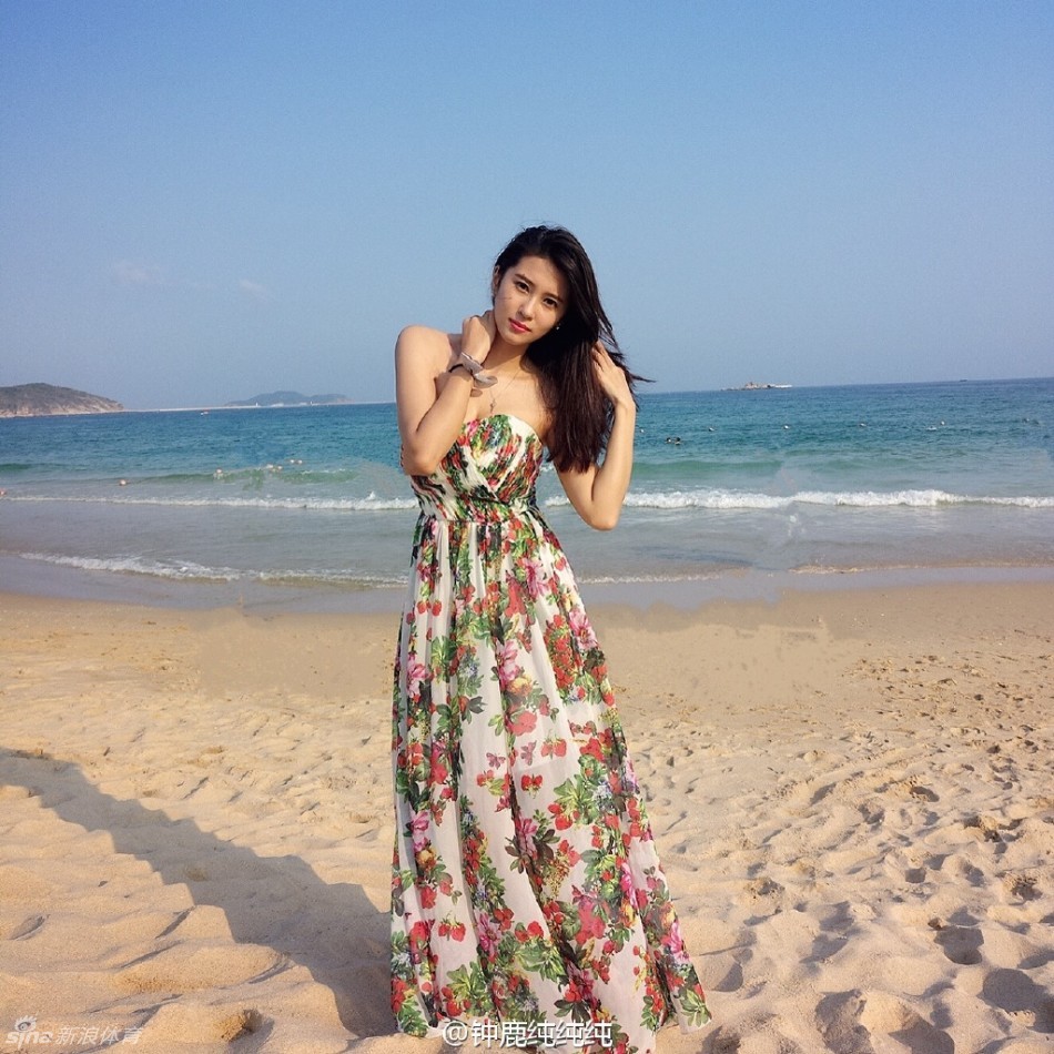 她身穿简约的白色连衣短裙，漫步在沙滩上，修长的双腿在蓝天碧海的映衬下显得格外耀眼，恰似一道流动的风景线。