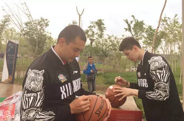 西热力江俯身给手中的篮球签名，他签得非常投入和细致，希望通过这颗篮球传递更多的爱心与正能量。
