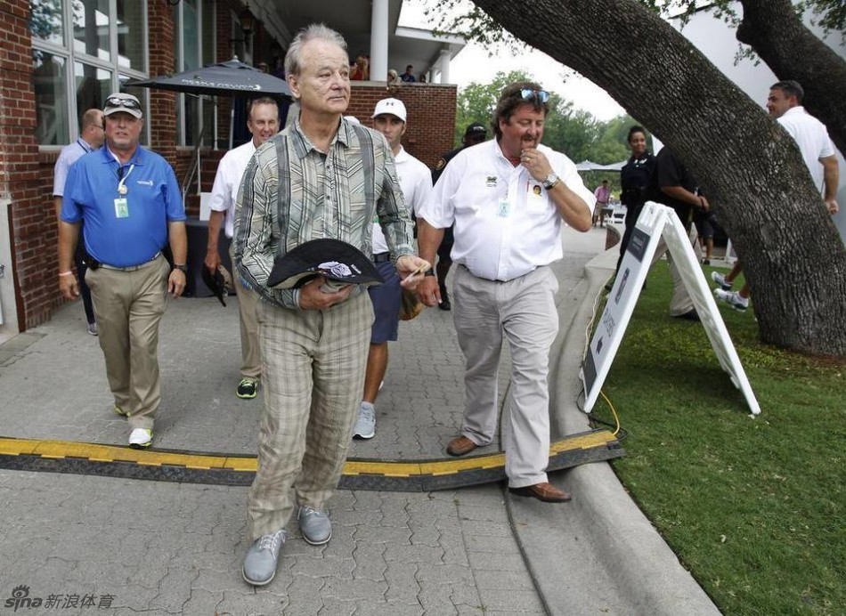 比尔·默瑞在果岭边缘进行切杆，他身体微微前倾，目光锁定在球与旗杆之间，姿势有模有样。