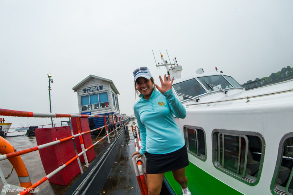 选手在临水练习场专注挥杆，小白球飞向远方，背景是开阔江面与盎然绿意