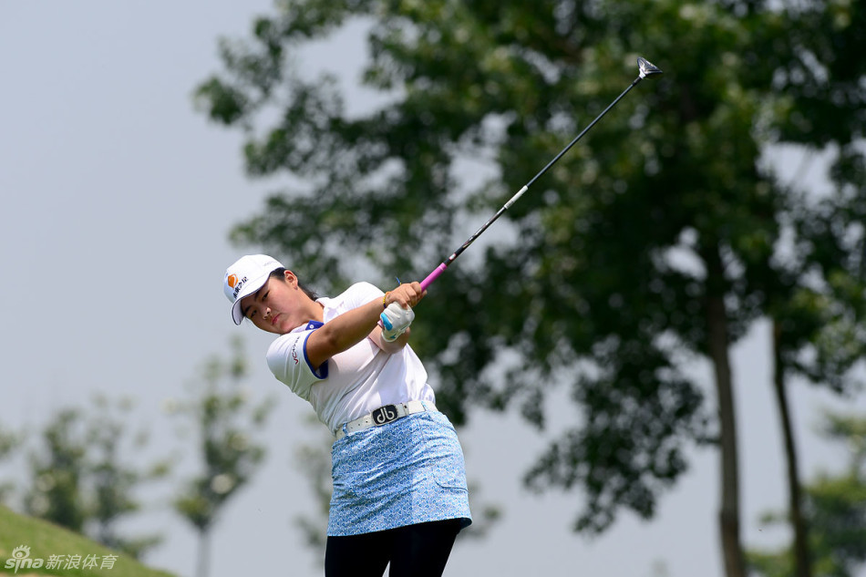 一位扎着马尾的少女高尔夫球手在发球台专注准备，她目光坚定地平视前方，双手稳稳握住球杆，身后是开阔的球场，整个姿态充满了力量与决心。