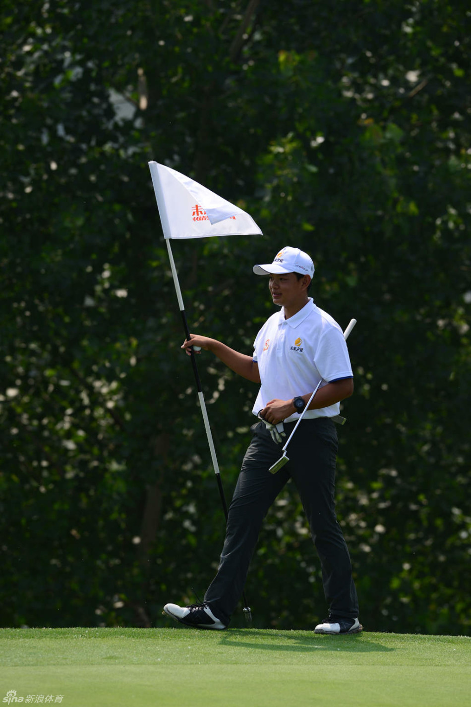 球员在果岭上进行长距离推杆，他刚刚完成推击动作，身体仍保持着送杆的姿势，目光紧盯着小球滚动的路线，神情专注而紧张。