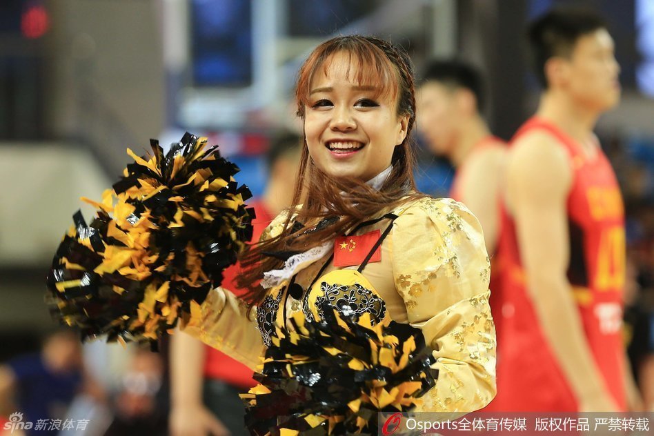 镜头拉近，两位篮球宝贝面对面站定，她们上身穿着白色紧身露脐背心，下身搭配蓝色热裤，展现出健康的小麦色肌肤和马甲线。她们正摆出一个充满力量感的定格姿势，眼神自信地望向远方的看台。