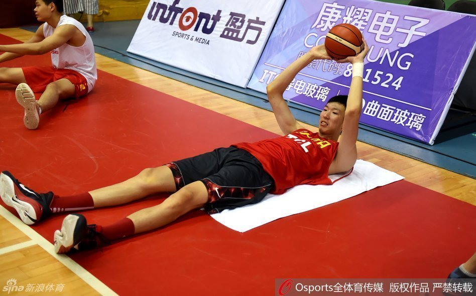 可兰白克侧身倾听，与穿着教练服的胡雪峰认真交流战术，眼神中充满对篮球的思考；身后的李慕豪正俯身进行腿部拉伸，肌肉线条清晰可见。