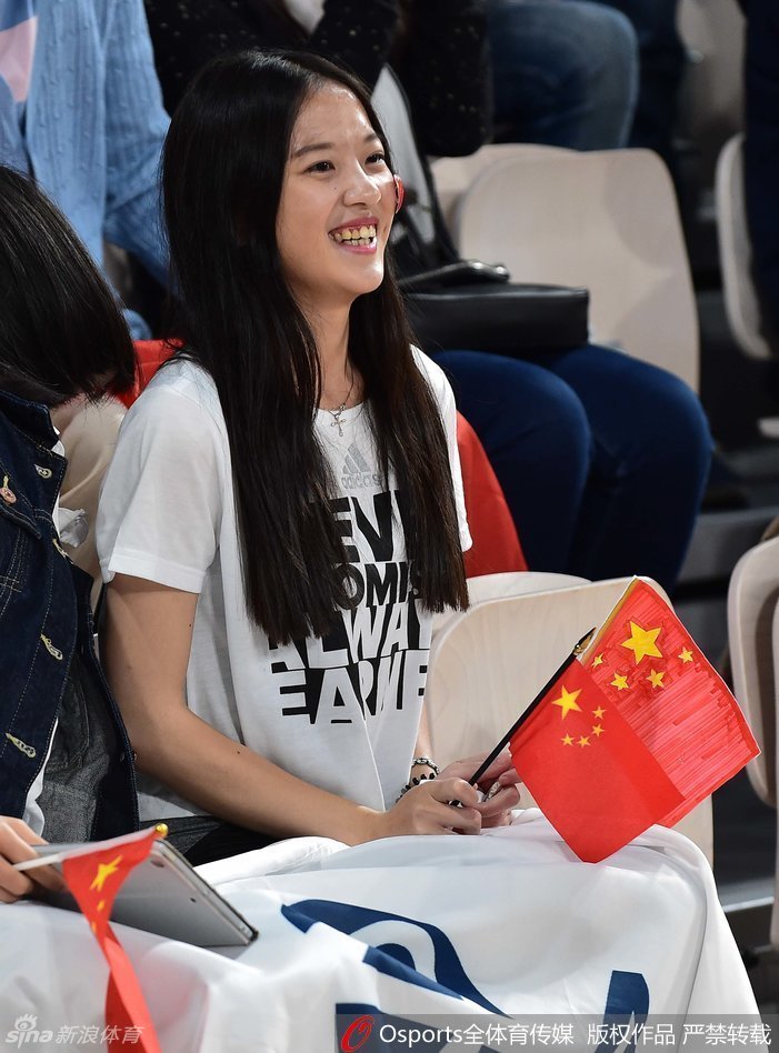 宽阔的体育馆看台上，众多手持五星红旗的球迷已经起身，他们面朝球场，脸上洋溢着紧张而兴奋的神情，仿佛要用自己的呐喊声穿透赛场，为正在进行赛前热身的女篮队员们传递力量。