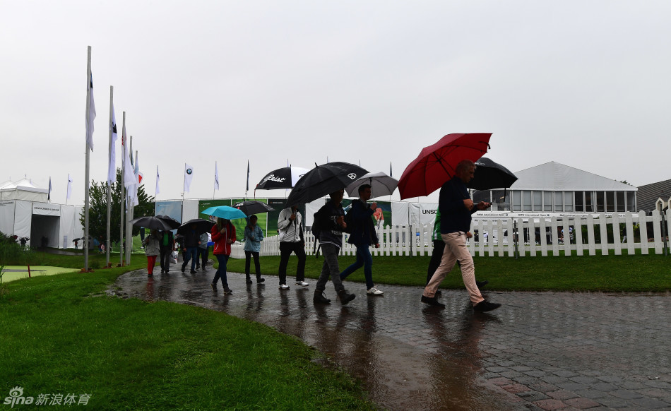 观众们聚集在赛场边临时搭建的遮雨棚下，目光投向被雨水笼罩的空旷球场