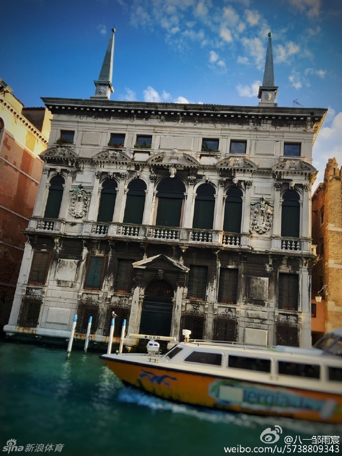 郭艾伦在威尼斯小巷中意外入镜，他手持拍摄设备神情专注，身后是色彩斑斓的威尼斯民居，成为画面中最生动的背景板。