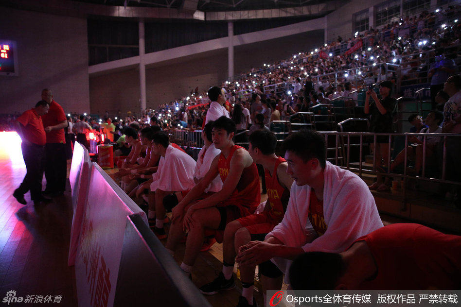 赛场全景图，明亮的灯光下是刚刚激战过的地板，而看台上星星点点的光芒尚未完全熄灭，记录下一场体育与温情交织的完美风暴。