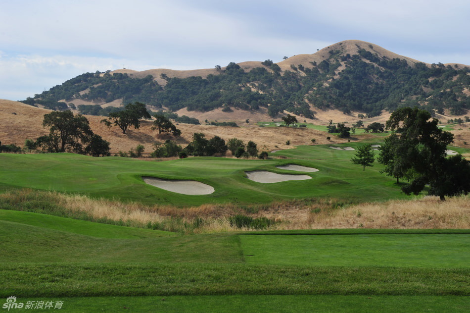 起伏的山地之上，球道如丝带般穿过茂密树林，展现着自然地形与人工设计和谐共生的壮丽景观