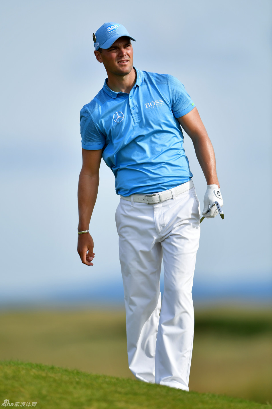 凯梅尔在长草区中，双腿稳稳站定，正全神贯注地执行一次困难的救球，杆头即将从浓密草丛中破草而出。