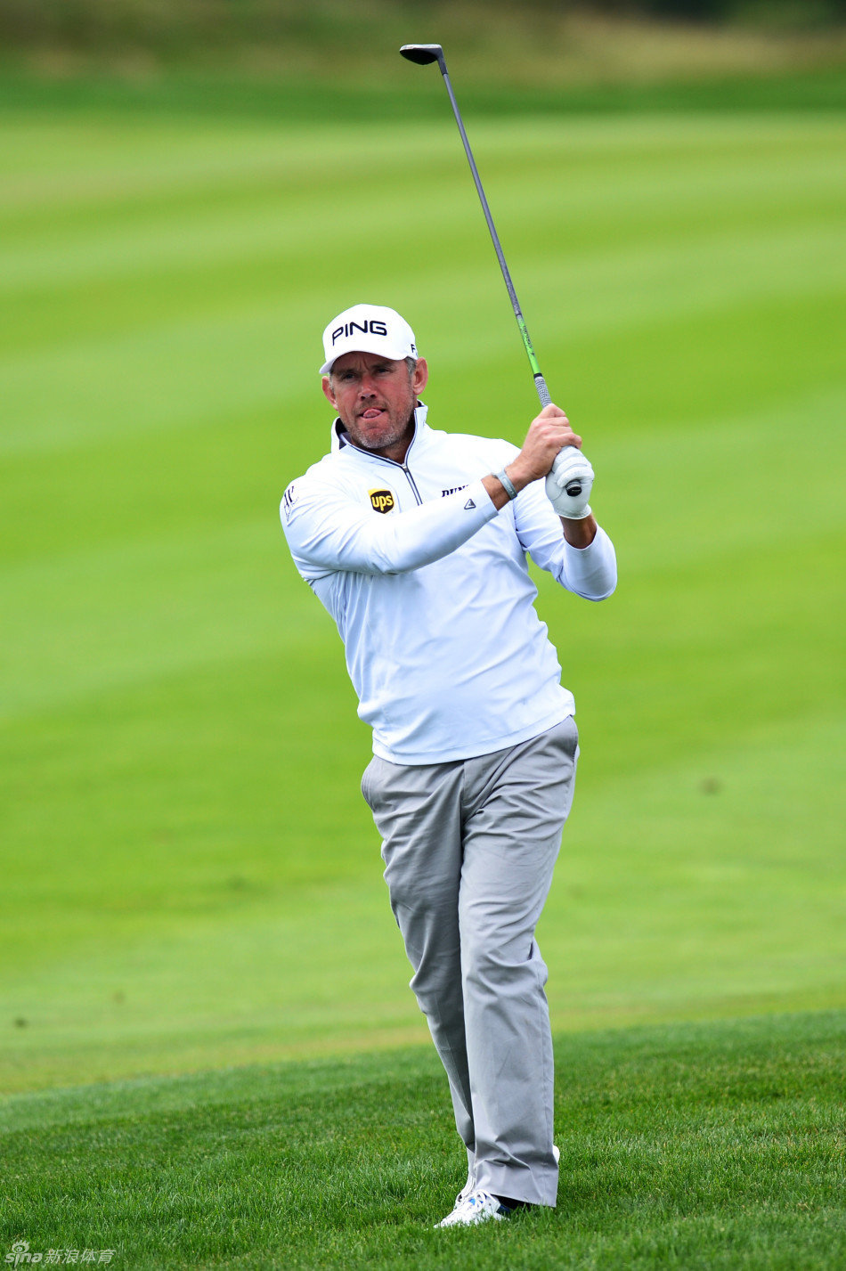 身着冠军绿夹克的彼得森站在领奖台中央，与身着红色上衣的赛事工作人员共同展示奖杯