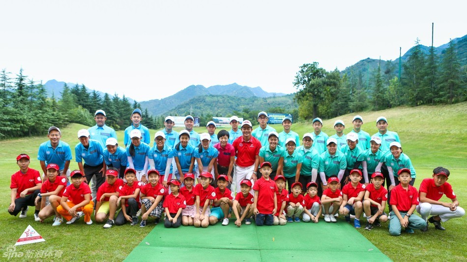 著名高尔夫球员梁文冲弯下腰，面带亲切笑容与一位年幼的小选手并肩合影，画面充满了鼓励与关爱。