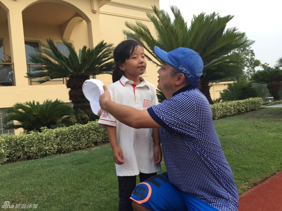 调皮的女儿举起帽子想要戴回爸爸头上，刘国梁配合地低下头，脸上满是纵容的笑意